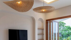 Ein modernes Wohnzimmer mit Flachbildfernseher, Korbtreleuchten, einem runden Couchtisch und einem großen Sofa.