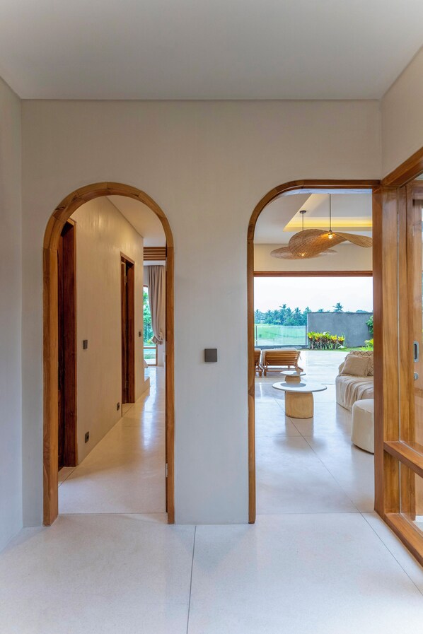 A modern interior with a hallway leading to a living area with a view of greenery.