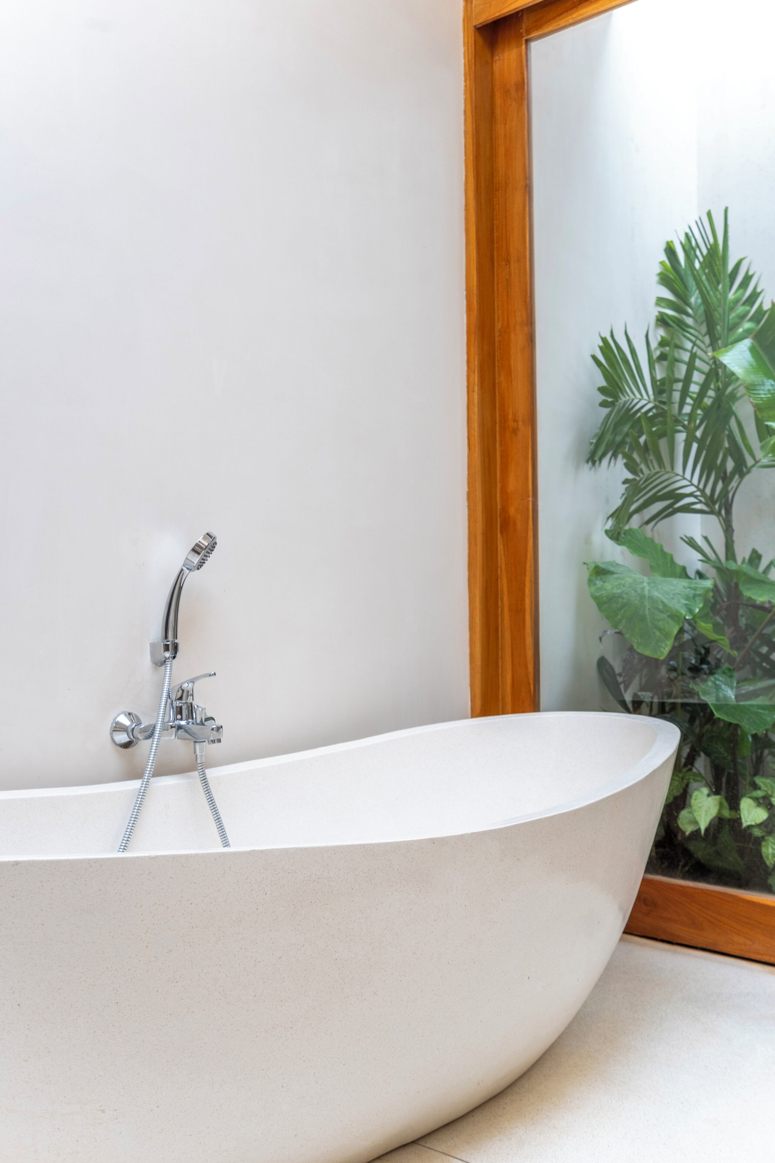 A modern bathroom with a freestanding bathtub, a wooden-framed mirror, and a potted plant.