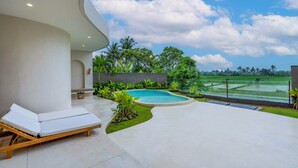 Ein moderner Poolbereich im Freien mit einer Liege, umgeben von Grün und Blick auf ein Reisfeld.