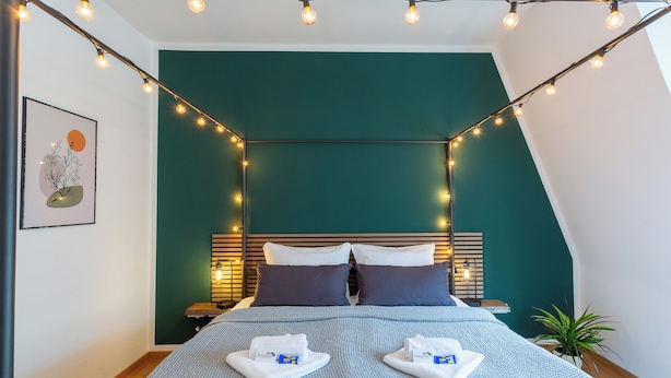 A neatly made bed with a blue patterned bedspread, two pillows, and two folded towels on the bed. - FeelgooD Apartment COZY Leipzig City-Center with underground parking space (Leipzig)