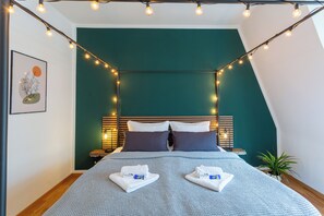 A neatly made bed with a blue patterned bedspread, two pillows, and two folded towels on the bed.