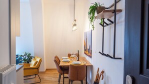 A dining area with a wooden table set for four, surrounded by brown chairs, a hanging light fixture, and a wall-mounted shelf with a plant. - FeelgooD Apartment COZY Leipzig City-Center with underground parking space (Leipzig)