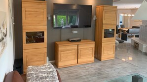 Uma sala de estar moderna com armários de madeira, uma televisão de tela plana e uma área de jantar com mesa e cadeiras.