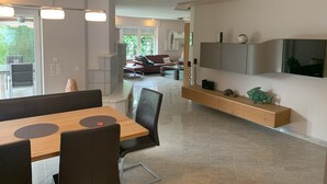 Uma sala de estar moderna com área de jantar, TV fixada na parede e lareira.