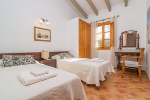 Ein Hotelzimmer mit zwei Betten, einem Nachttisch aus Holz, einem Spiegel, einem Fenster mit Vorhängen und einem Fliesenboden.