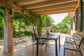 Eine Terrasse im Freien mit Tisch und Stühlen, umgeben von Pflanzen und einem gefliesten Boden.