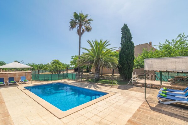 Ein rechteckiger Pool mit gefliestem Sonnendeck, umgeben von Liegestühlen und einer überdachten Sitzgruppe.