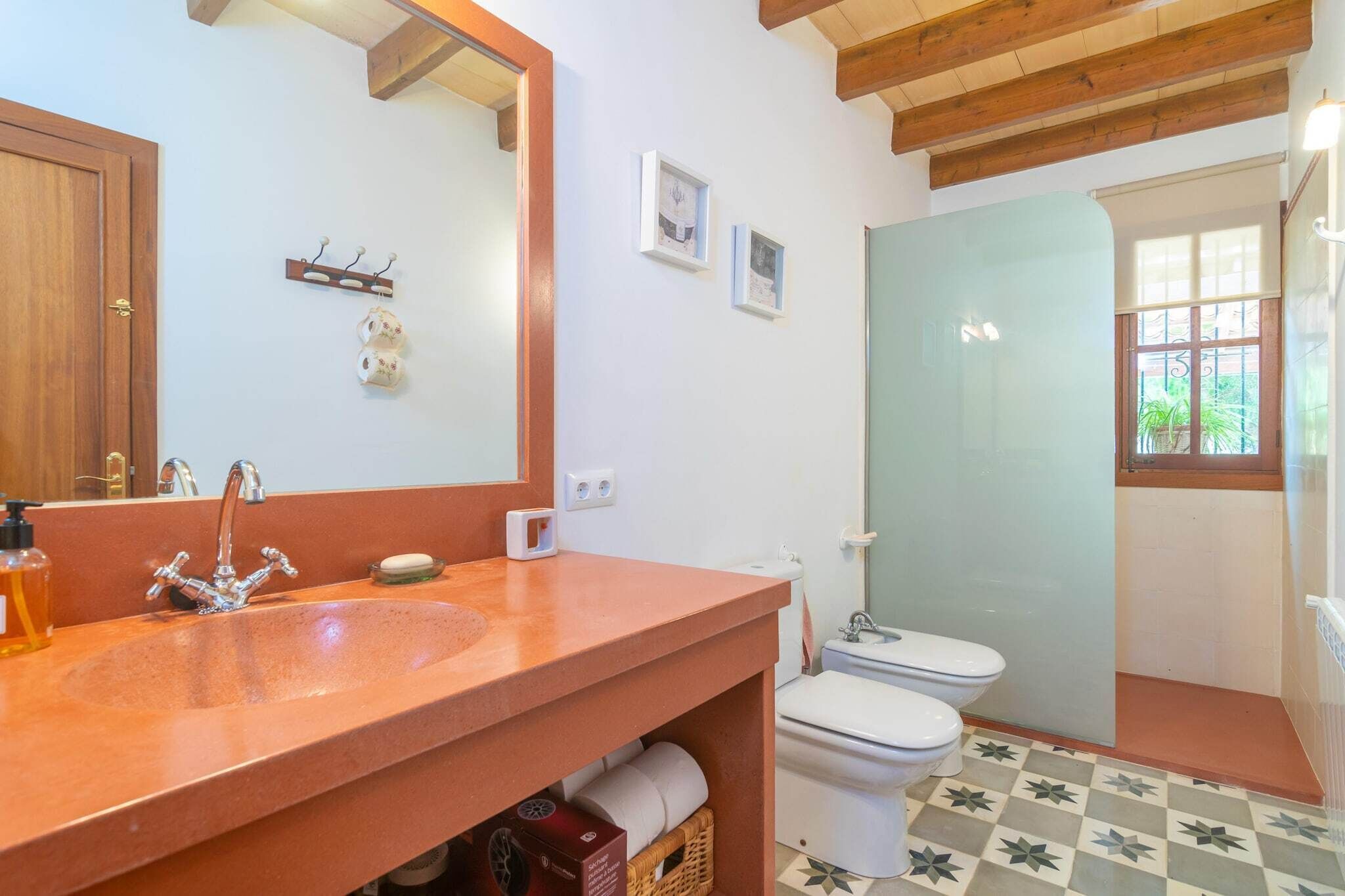 A bathroom with a wooden ceiling, a sink with a mirror, a toilet, and a shower area.