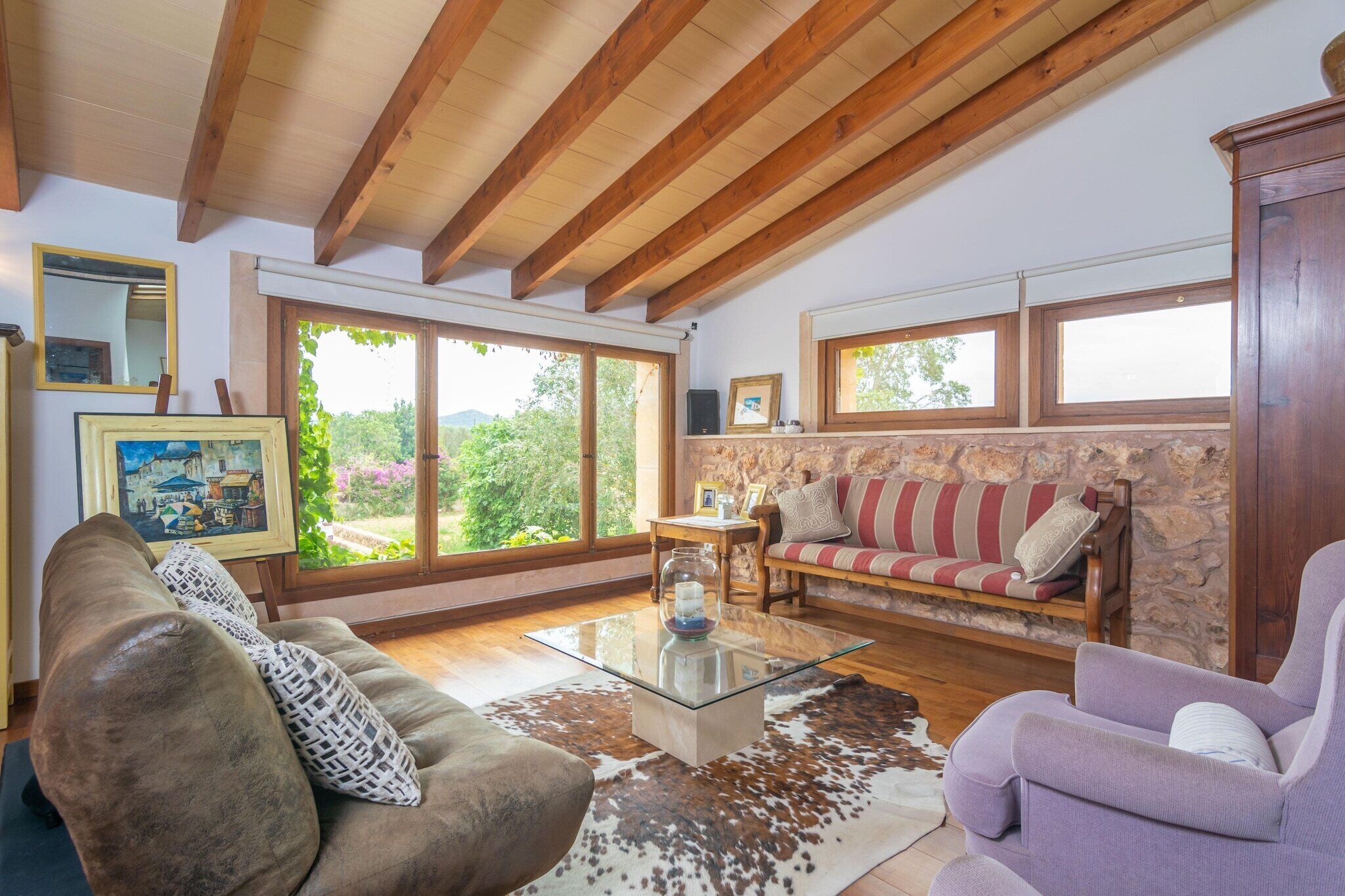 A spacious living room with a glass coffee table, leather sofas, and a stone wall.