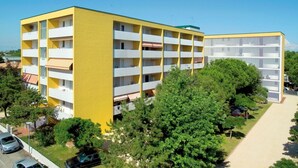 A multi-story yellow building with balconies, surrounded by trees and a clear sky. - Modern studio in the heart of the city (Bibione)