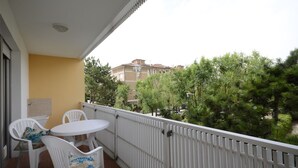 A balcony with a white table and chairs, a yellow wall, and a view of trees and buildings. - Modern studio in the heart of the city (Bibione)