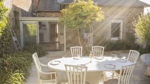 A round table with white chairs in a courtyard, surrounded by plants and a stone building. - Large house 80m from the port (Paimpol)