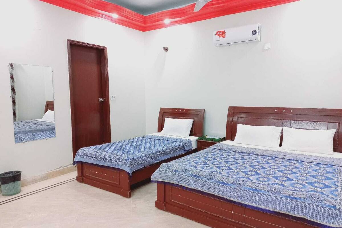 A room with two wooden beds, a ceiling fan, a wall-mounted air conditioner, and a door.