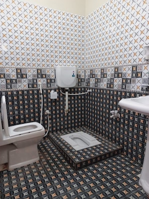 Une petite salle de bain comprenant des toilettes, un bidet et un lavabo. Les murs sont recouverts de carreaux disposés selon un motif géométrique.