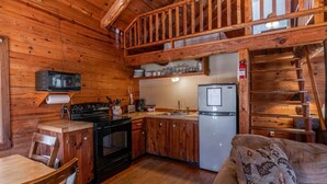 Interior de una cabaña de madera con cocina, comedor y escalera.