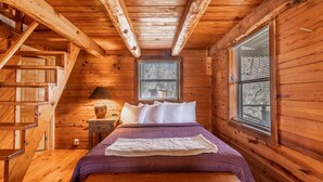 Un dormitorio tipo cabaña de madera con una cama, una mesita de noche, una lámpara y una ventana con persianas.