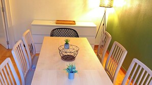 Un comedor con una mesa blanca, seis sillas, una planta pequeña en maceta y un letrero colgado en la pared.