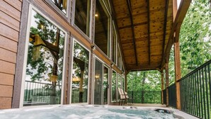 Wellnessbereich mit Whirlpool, Holzterrasse und großen Fenstern mit Blick auf einen Wald.