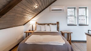 Ein Schlafzimmer mit schräg gedachter Decke, einem Bett mit weißer Bettwäsche, zwei Nachttischen, einer Wandkonsole und zwei Fenstern.