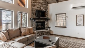 A living room with a stone fireplace, leather sofa, and a coffee table. - The Foxfire Cabin - Tree-top Getaway (Ponca)