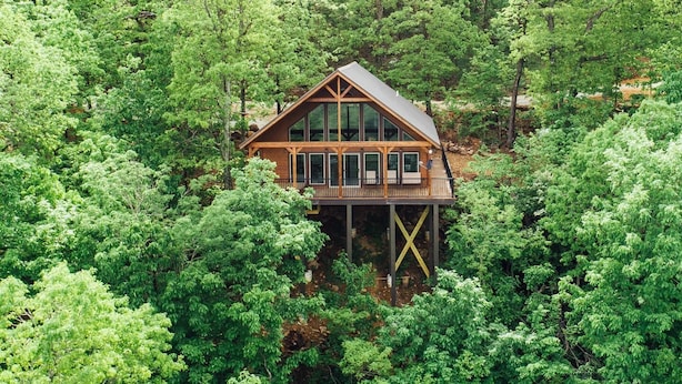 A wooden cabin with large windows and a deck, surrounded by dense forest. - The Wildwood Cabin - Tree-top Getaway (Ponca)
