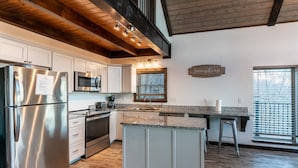 A modern kitchen with stainless steel appliances, white cabinetry, and a large island. - The Wildwood Cabin - Tree-top Getaway (Ponca)