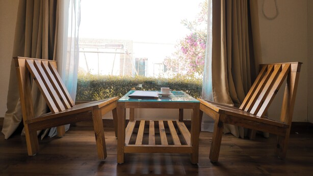 Una habitación con una mesa de madera y dos sillas, una ventana con cortinas y vistas al exterior con vegetación.