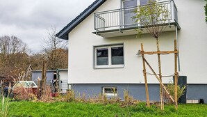 A two-story house with a balcony, a small garden, and a shed in the background.
