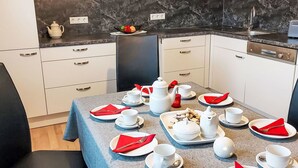 A modern kitchen with white cabinets, a marble backsplash, and a dining area set with white plates, red napkins, and white cups.
