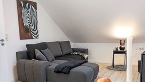 En moderne stue med en grå hjørnesofa, et rundt træbord med æbler, et hvidt stearinlys og et billede af en zebra på væggen.