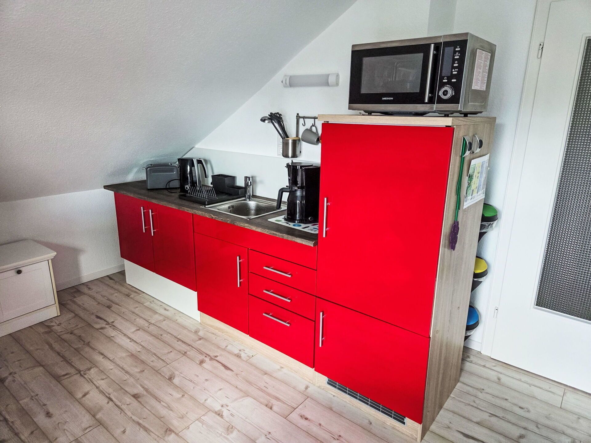 Una cocina compacta con gabinetes rojos, un microondas, un hervidor y un lavamanos.