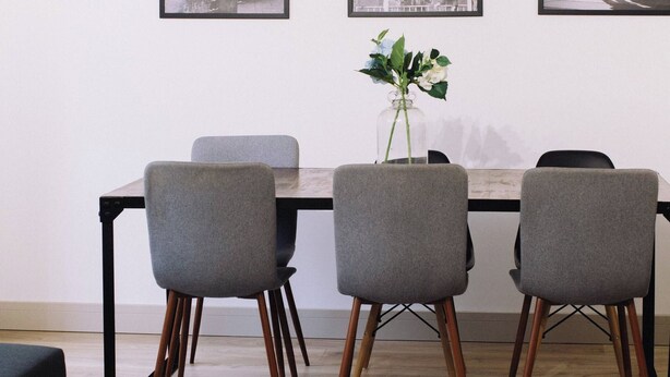 Un comedor con una mesa, cuatro sillas grises, un jarrón con flores y fotografías blanco y negro enmarcadas en la pared.