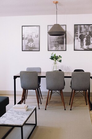 Un comedor con una mesa, cuatro sillas grises, un jarrón con flores y fotografías blanco y negro enmarcadas en la pared.