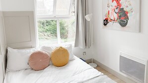 Un dormitorio con cama, ventana, radiador y un cuadro de una mujer en un patinete.