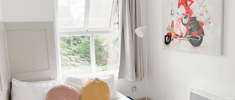 Une chambre à coucher avec un lit, une fenêtre, un radiateur et un tableau représentant une femme sur un scooter.