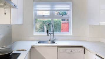 Een keuken met witte kastjes, een raam met uitzicht op groen, een roestvrijstalen spoelbak en een vaatwasser.