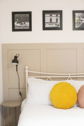 A bed with white and yellow pillows, a bedside lamp, and framed pictures on the wall. - Entire 2 Bedroom House 7m To Station (Barnet)