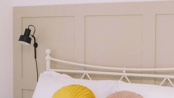 A bed with white bedding and two decorative pillows, a white headboard, and a wall-mounted lamp.