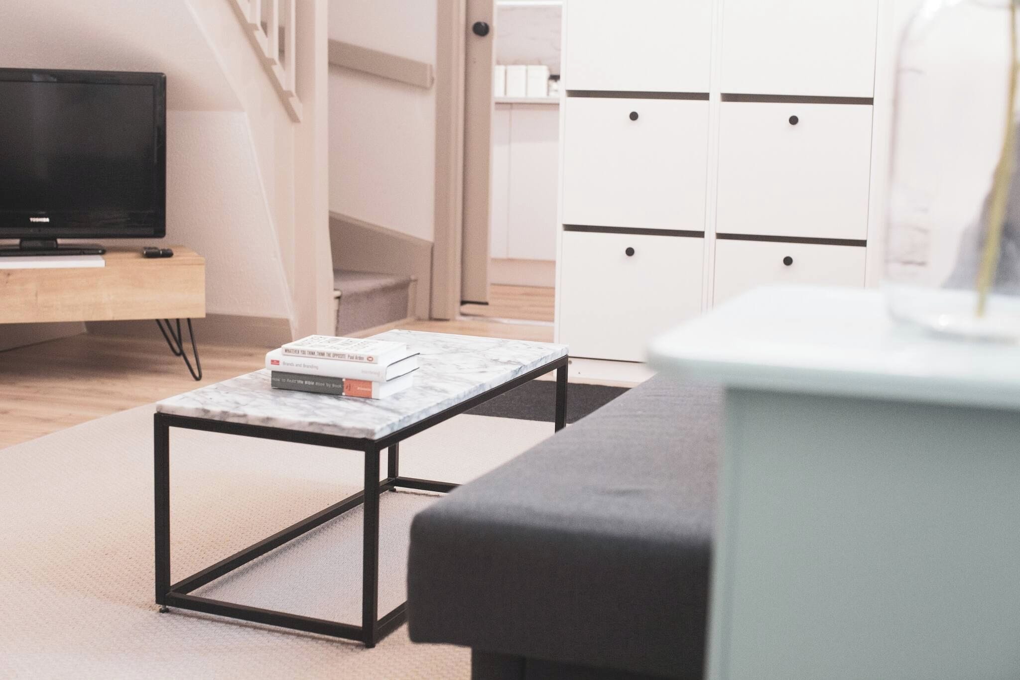 Un salon moderne avec un téléviseur à écran plat, une petite table basse sur laquelle repose un livre, un canapé et un meuble blanc avec des tiroirs.