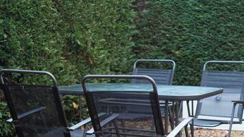 Een terras met metalen tafels en stoelen, omgeven door een haag en een grindpad.