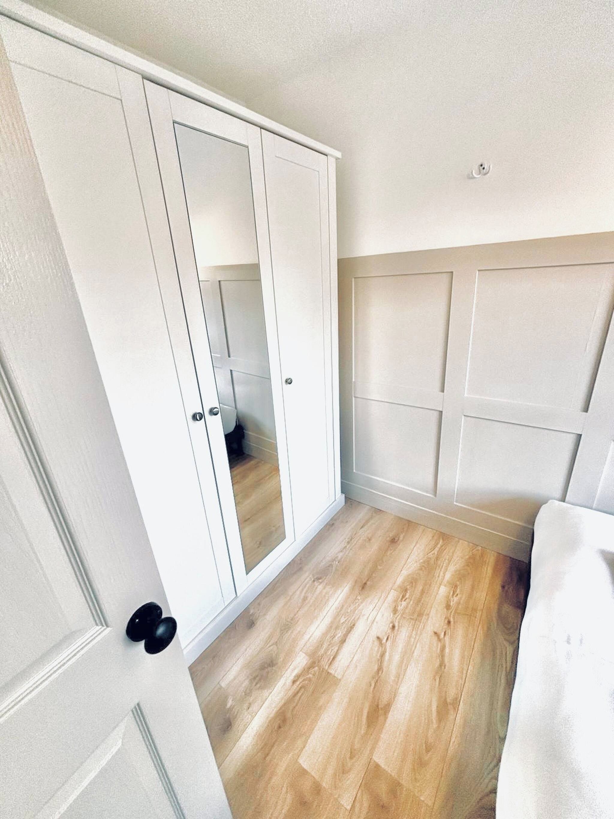 A room with a wardrobe, a bed, and a wooden floor.