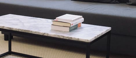 Una sala moderna con un sofá gris, dos cojines grises y una mesa de centro de mármol con libros.