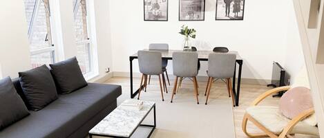 A modern living room with a grey sofa, a coffee table, a dining table with chairs, and framed pictures on the wall.