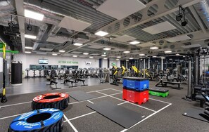 Un gimnasio con equipo de ejercicio variado, un saco de boxeo y un letrero motivacional en la pared.