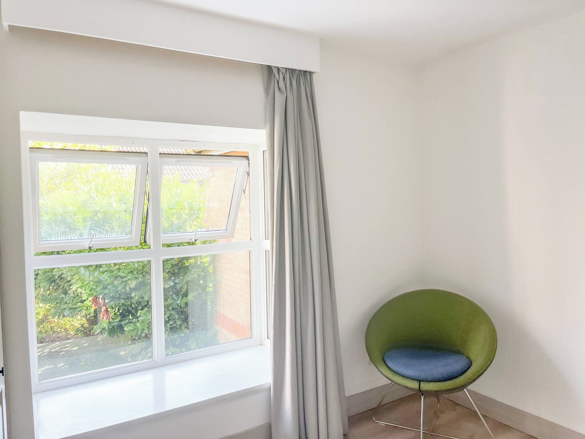 Une pièce avec une fenêtre, un fauteuil vert et un rideau.
