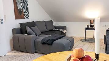 Ein modernes Wohnzimmer mit einem grauen Ecksofa, einem runden Couchtisch mit Äpfeln, einer weißen Kerze und einem Zebra-Gemälde an der Wand.