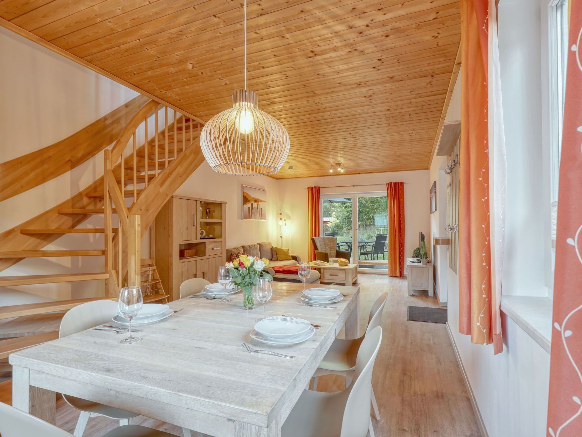 A dining area with a wooden table set for four, a staircase, and a kitchen in the background.