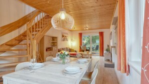 Un coin repas avec une table en bois dressée pour quatre personnes, un escalier et une cuisine en arrière-plan.
