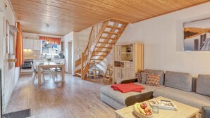 Un vaste espace de vie comprenant un escalier en bois, une table à manger avec des chaises, un canapé et une table basse sur laquelle sont disposés des fruits.